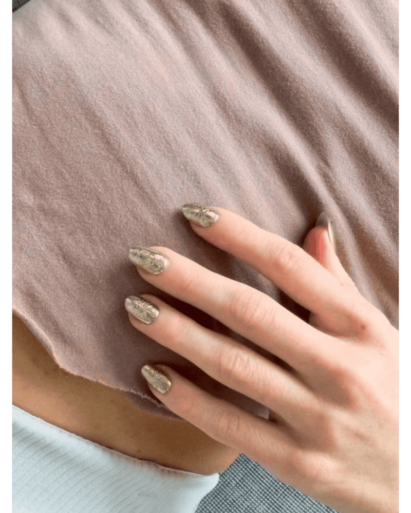 Hand resting on a dusty rose fabric showing gold foil press-on nails from the Rave Nailz Gilded Gold collection